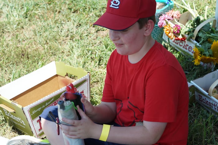 Boy in read shirt sitting in the shade with a water bottle and usb powered fan hooked to an iphone