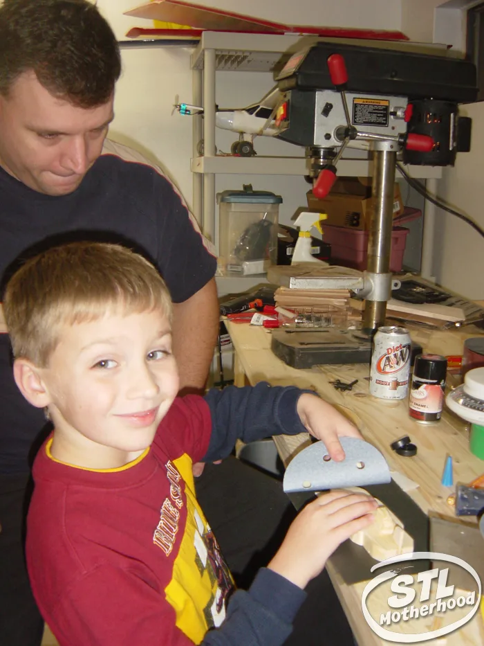 Boy and his dad in a home workshop making a pinewood derby car