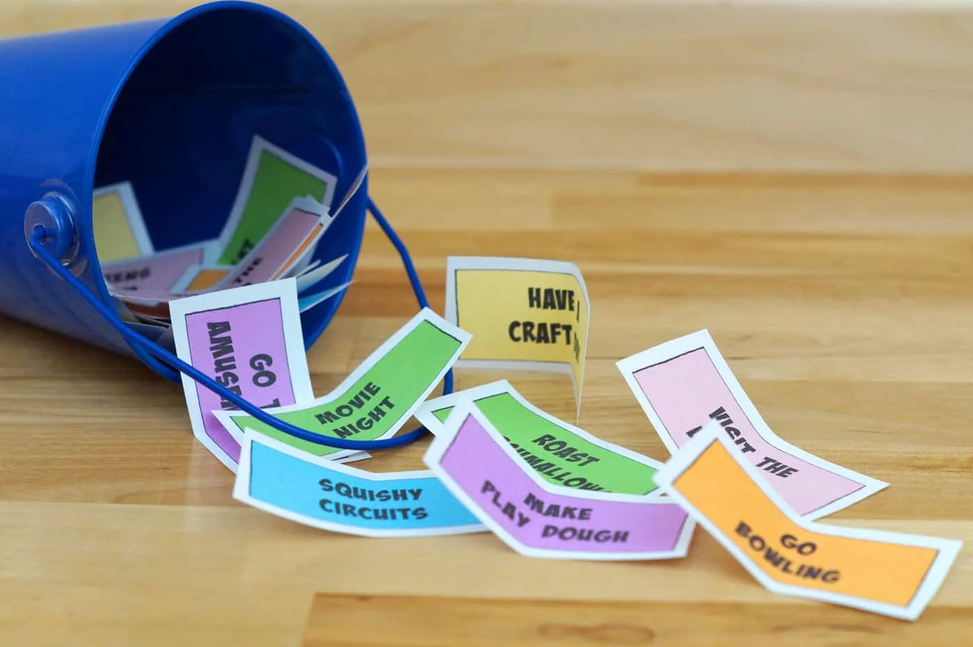small blue bucket full of color paper with kid activities printed on them