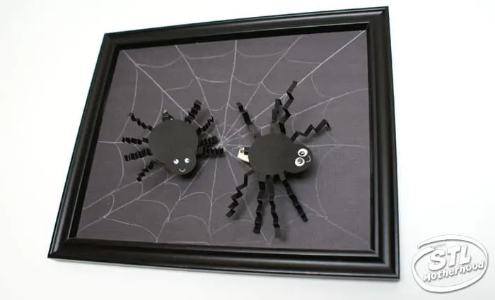Halloween Brush Bot dressed as spiders on a picture frame with a web.