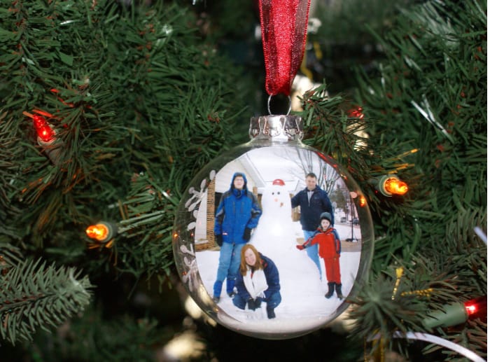 Family photo next to snowman in a glass ornament hung on a Christmas tree