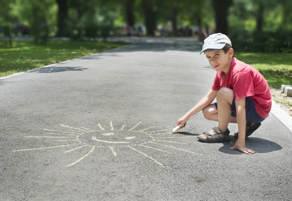 Child drawing sun on asphalt in a park