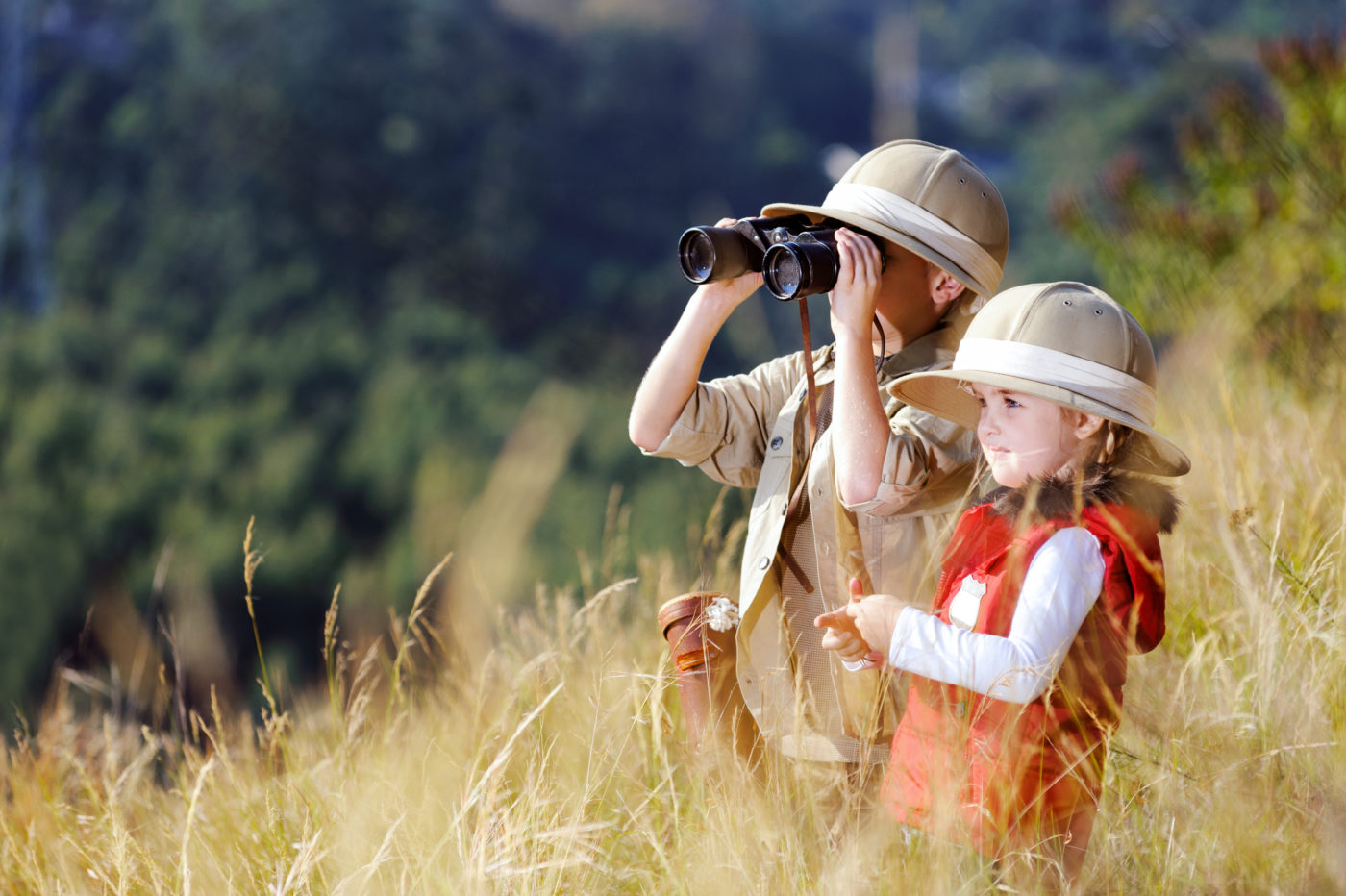 Children brother and sister playing outdoors pretending to be on safari and having fun together with binoculars and hats