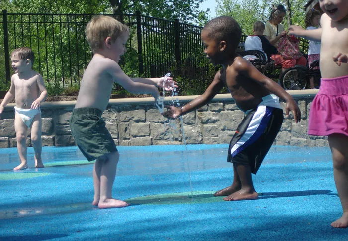 Two preschool boys in swim trunks--one white, one African American--make friends at a splash pad in the Children's Garden at the Missouri Botanical Garden.