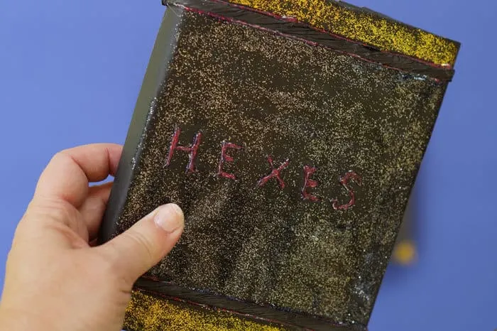 Black book cover with gold glitter, title says Hexes in red glue
