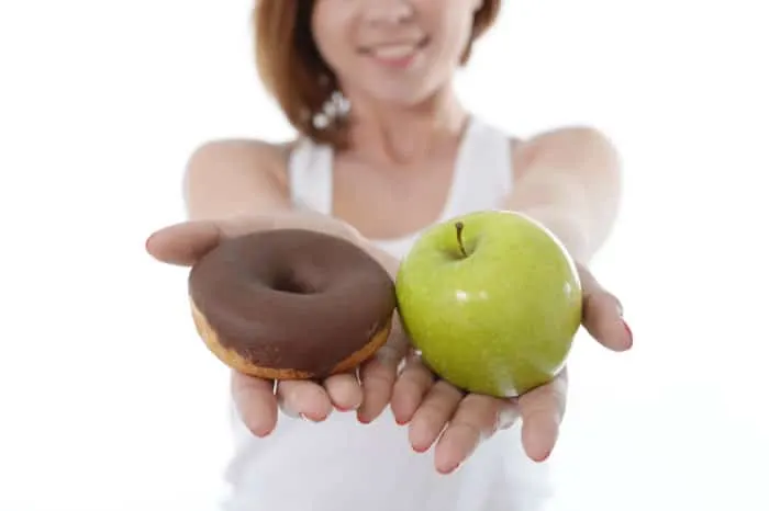 Young sport Woman with Apple and Chocolate Donut in Hands to choose