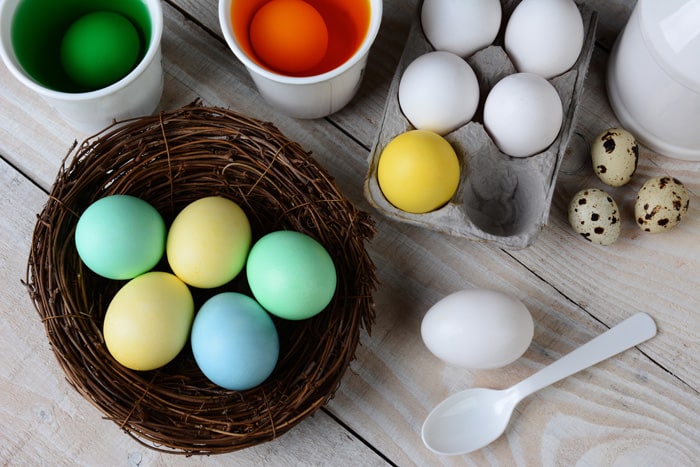 High angle view of Dying Easter Eggs. Dyed eggs in a nest with eggs in dye solution and other eggs ready to be dunked. Horizontal format on a rustic farmhouse style kitchen table.