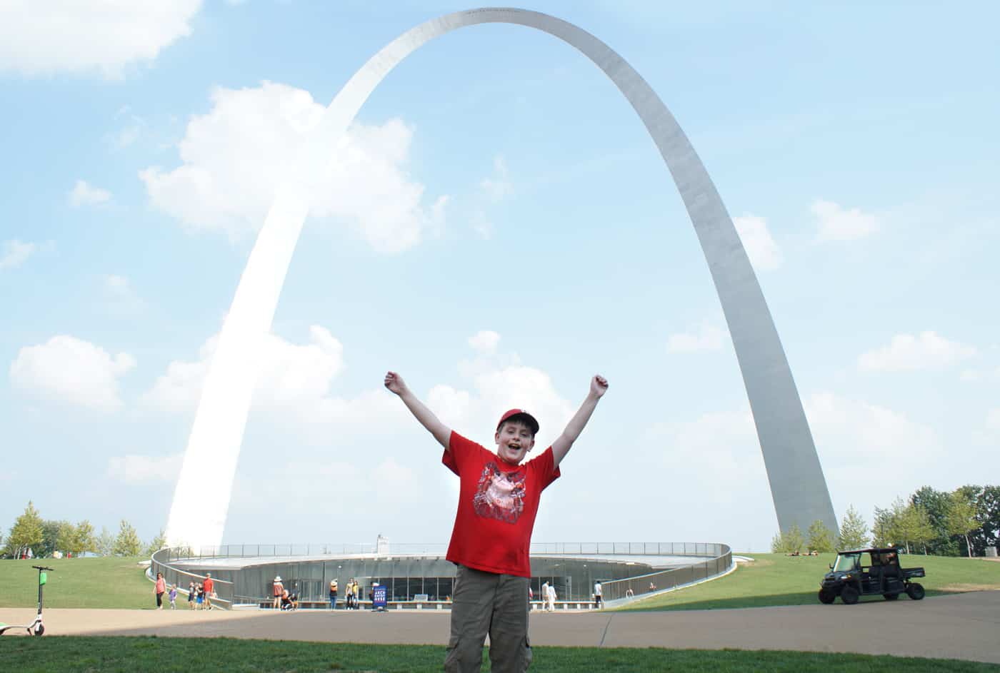 boy standing with arms up by the Gateway Arch in St. Louis