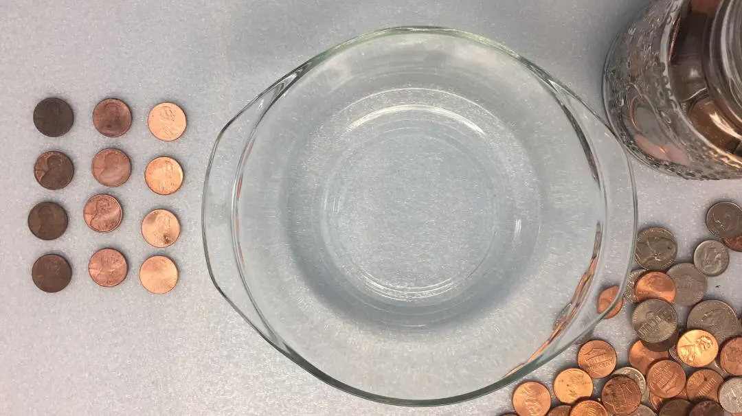 pennies set out for cleaning next to a bowl of vinegar and salt