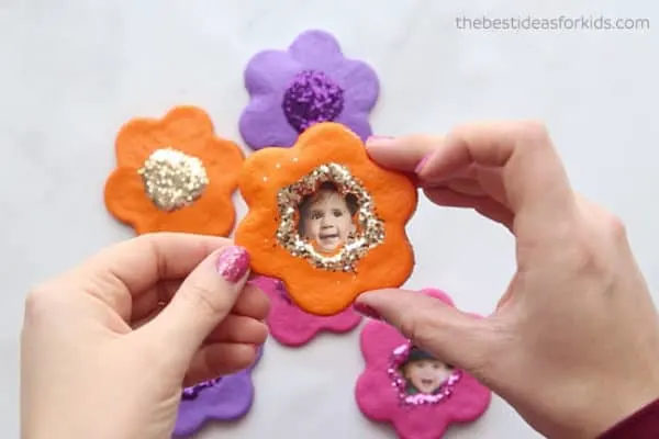 cookie cutter flowers made from salt dough and turned into magnets--painted, glittered and has a kid's picture in the middle
