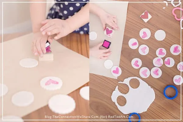 Child's hands using rubber stamp to make heart stamped clay magnets.
