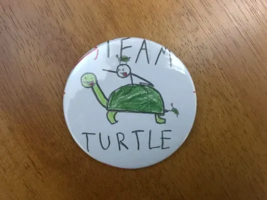 Button that reads "Team Turtle" with child's drawing of a stick man riding a turtle.