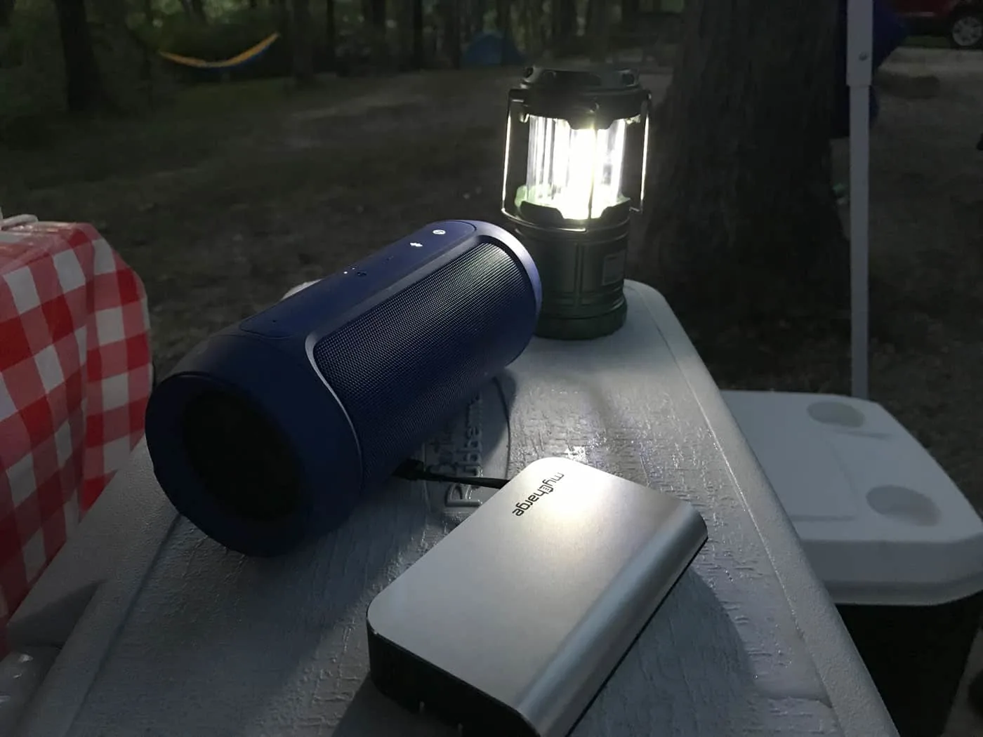 myCharge power bank on a cooler, plugged into a blue portable can speaker, camping lantern in the background.