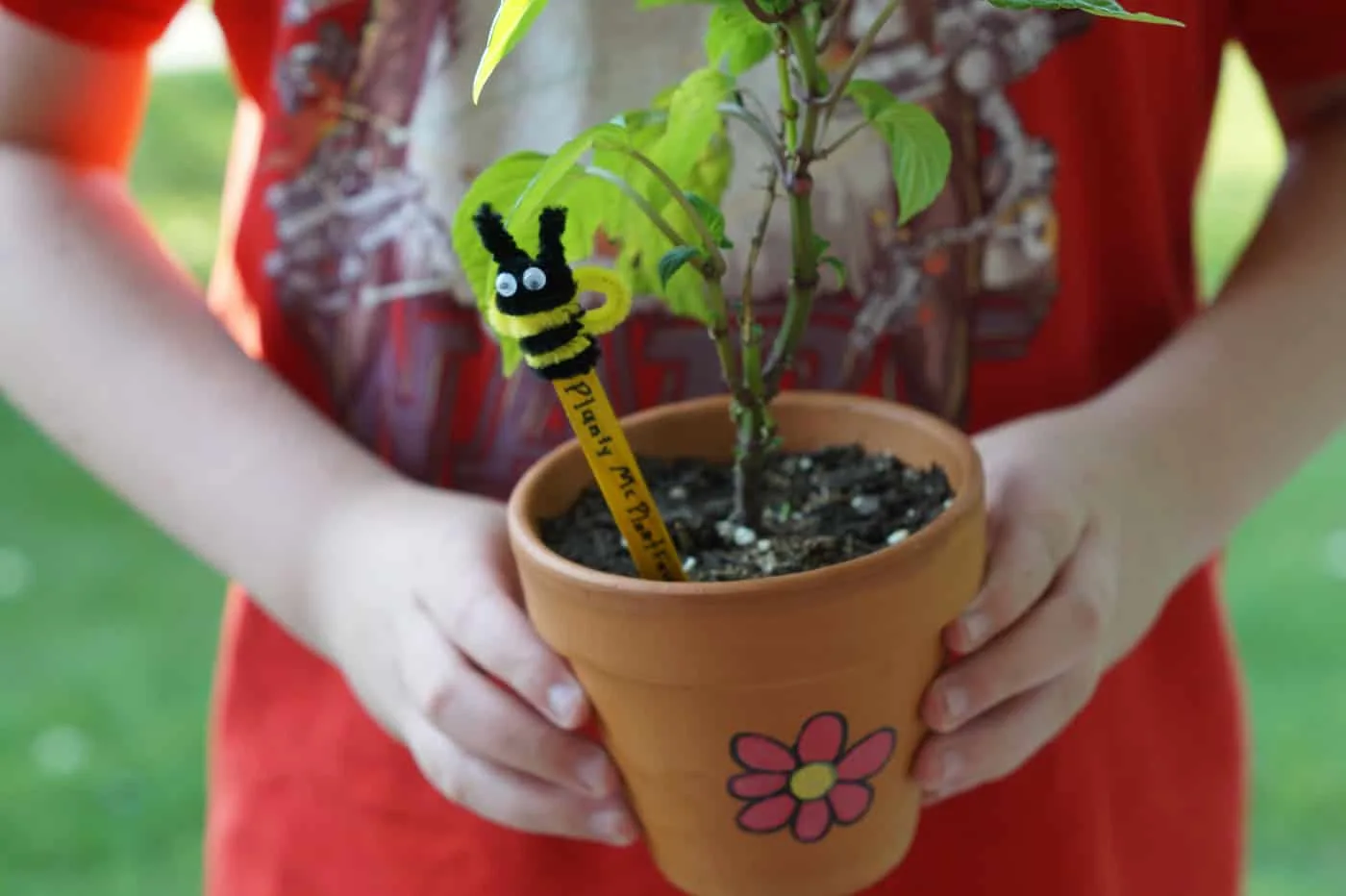 kid holding a potted plant with a bee garden marker. Planty Mc Plantface is written on the marker.