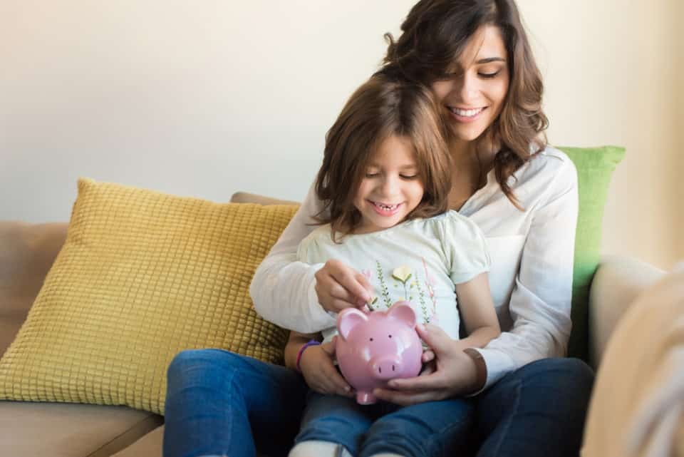 Mother and daughter putting coins into piggy bank