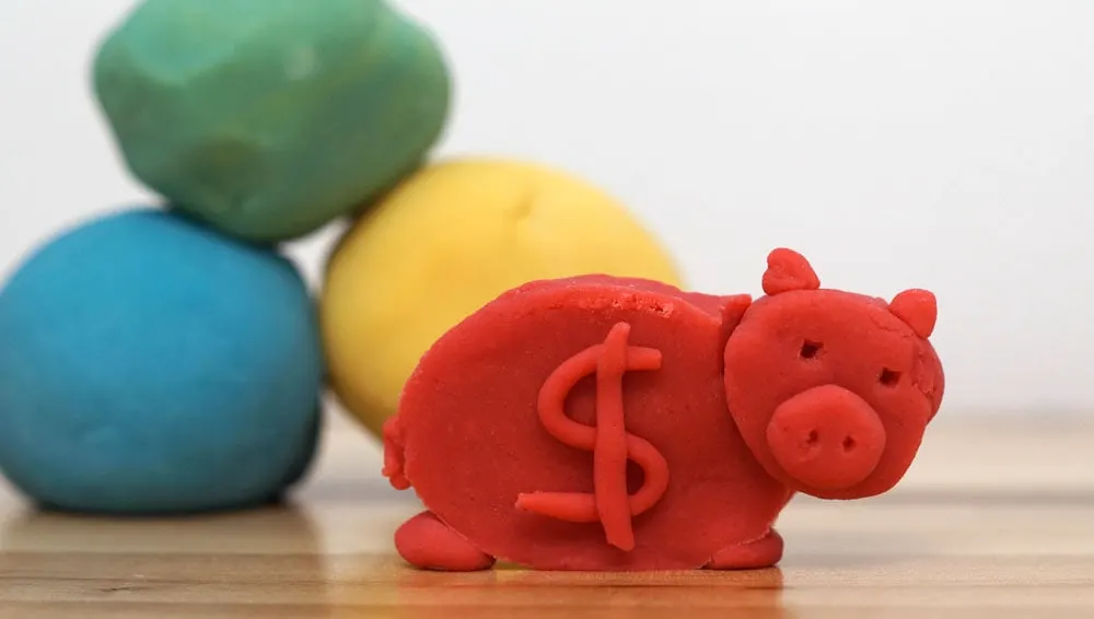 Play dough piggie bank in red with balls of green, blue and yellow dough in the background