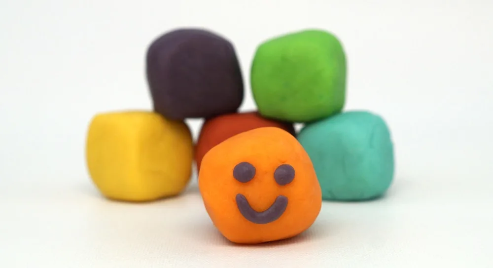 blocks of home made play dough in rainbow colors, the orange one has a smiley face