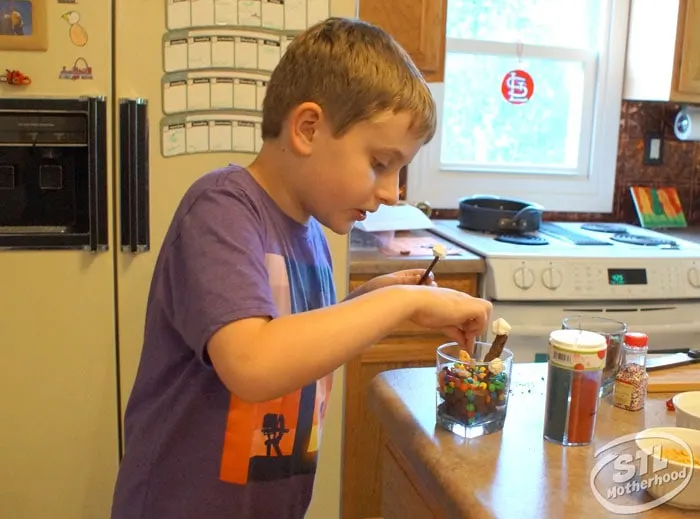 Kid in kitchen preparing "dirt" cup for STEM experiment. Dirt is made of crushed cookies and candy.