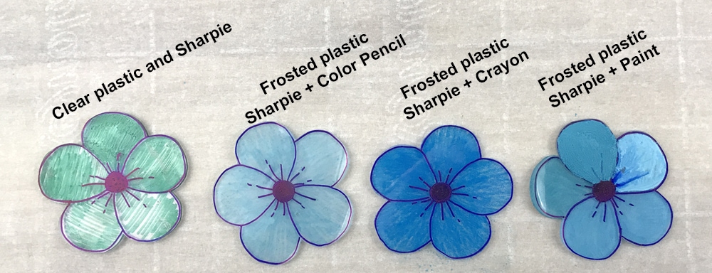 blue shrinky dink flowers colored in different mediums: sharpie, colored pencil, crayon, and paint