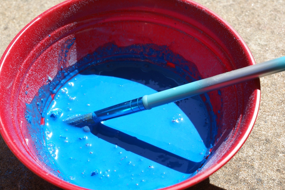 bowl of sidewalk chalk paint with a brush used to stir it