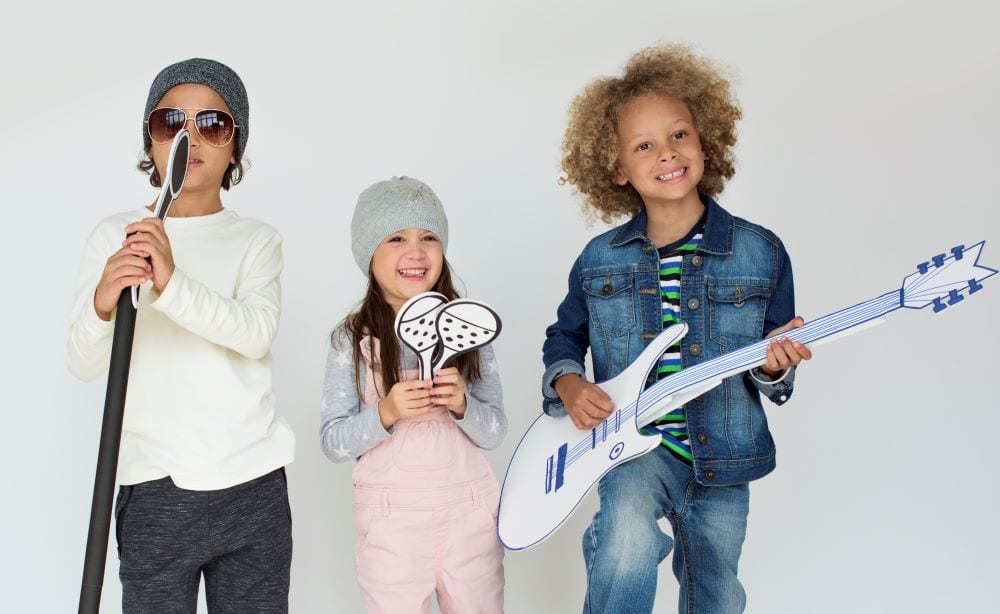 three kids playing with paper cut out instruments 