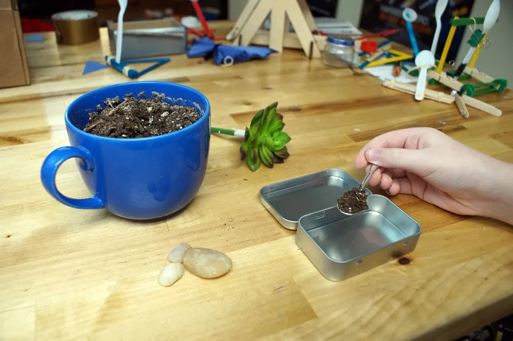 putting dirt in a tin with a tiny spoon