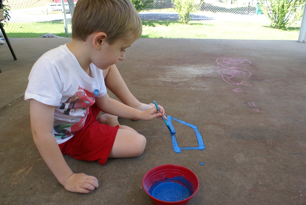 preschool boy painting outside with homemade blue sidewalk chalk paint