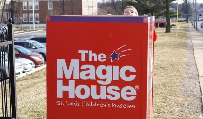 Kid peeking out behind the red Magic House sign