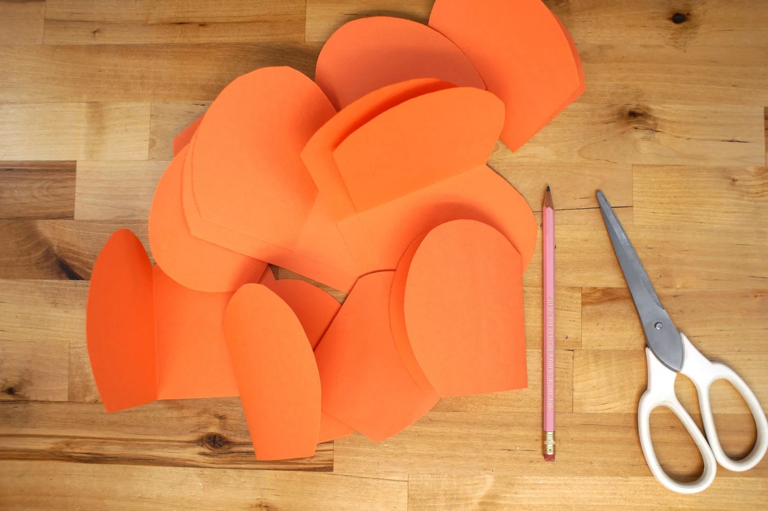 paper pumpkin slices cut from orange construction paper with pink pencil and a pair of scissors.