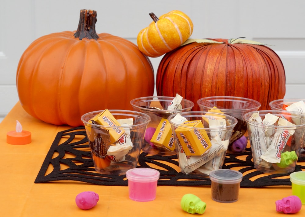 Halloween candy in clear cups on a table with pumpkins for trick or treating