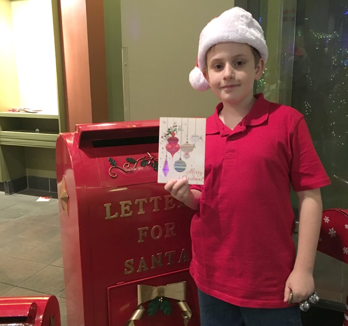 kid holding a santa letter next to a red Letter to Santa mailbox