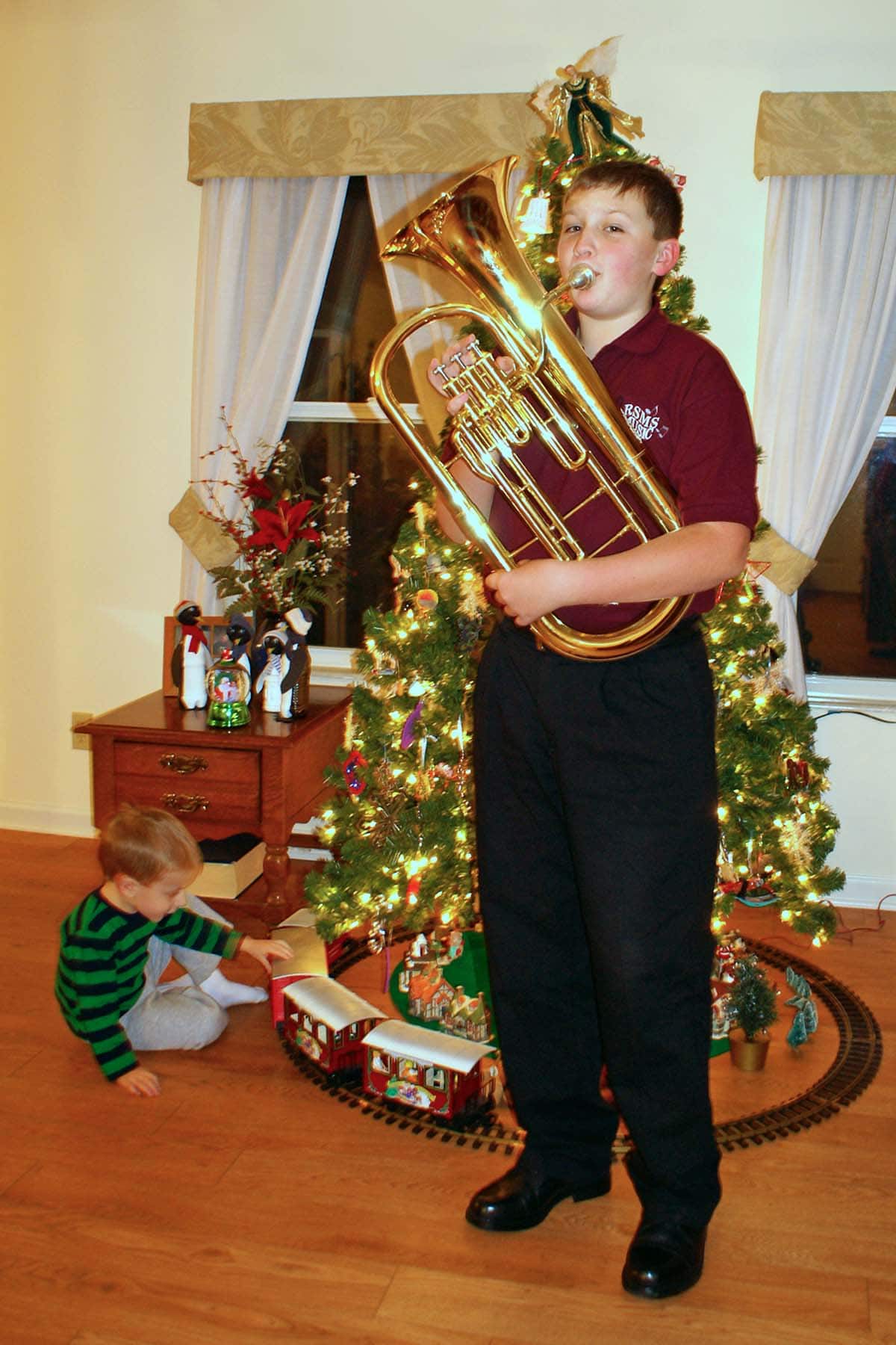 Kid in school polo with brass baritone horn in from of a Christmas tree.