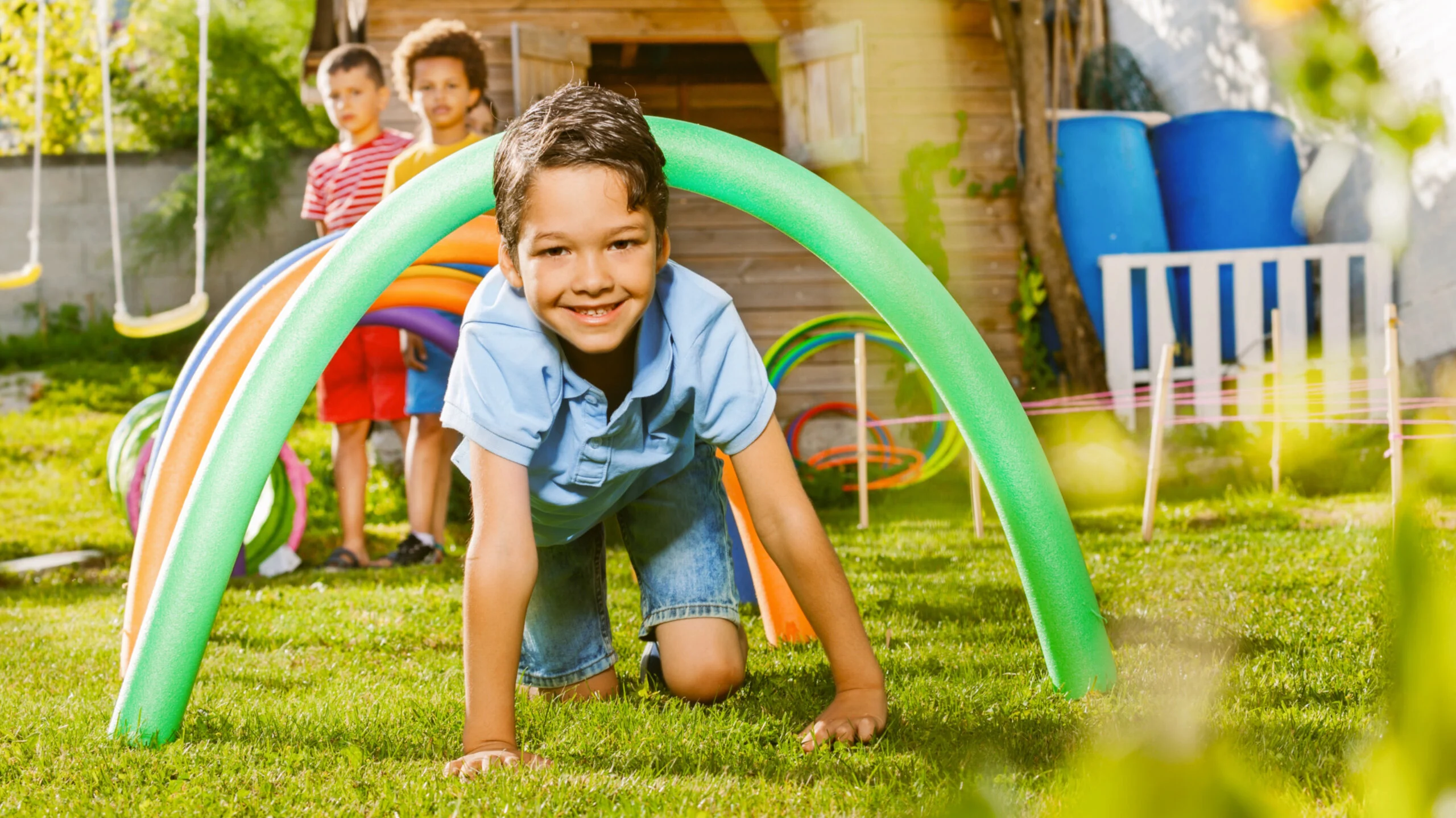 Kids crawl under pool noodles in a backyard game
