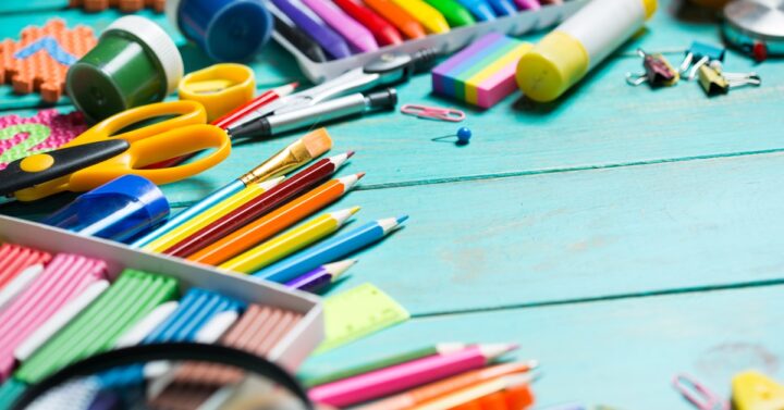 Colorful pencils, scissors, markers, and craft supplies cover a turquoise table during a kid craft supply swap.