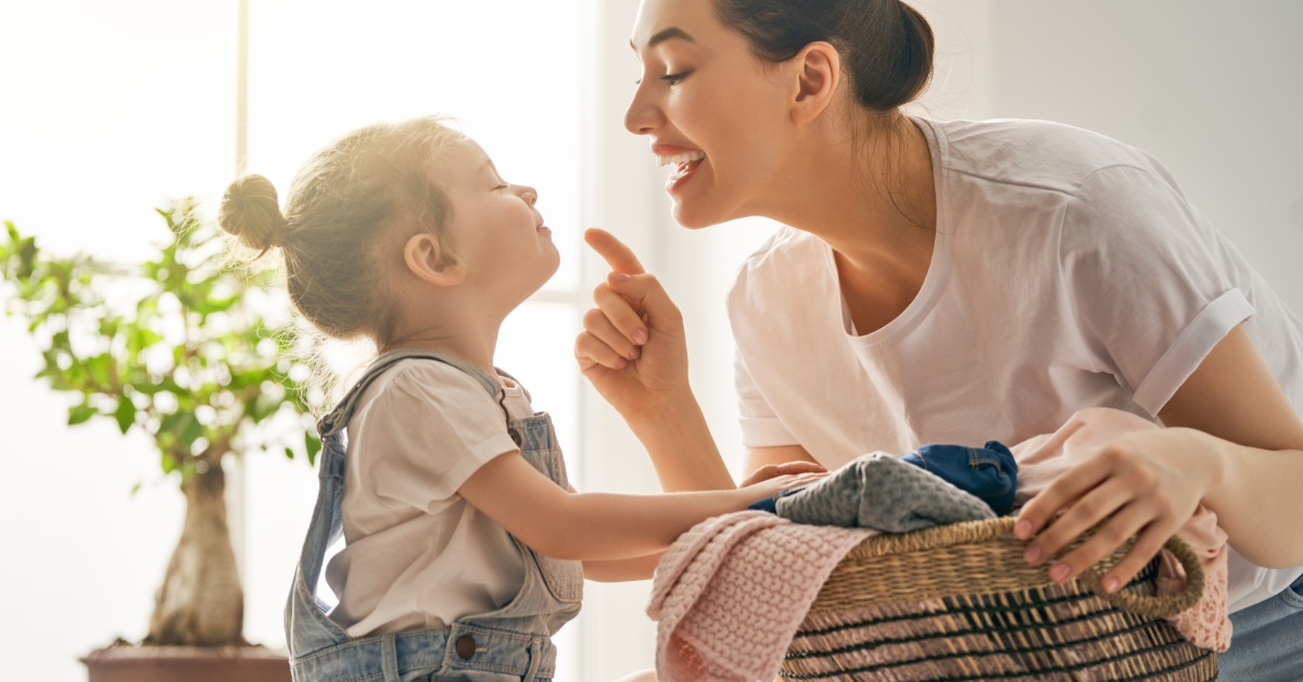 A woman and her small child are looking at each other, face to face. The mother is carrying a basket.
