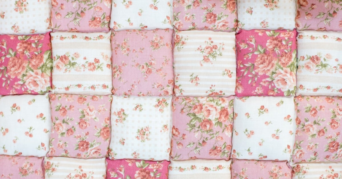 Close-up of a pink puff quilt featuring rose-print fabric squares, delicate floral patterns, and pale stripes.